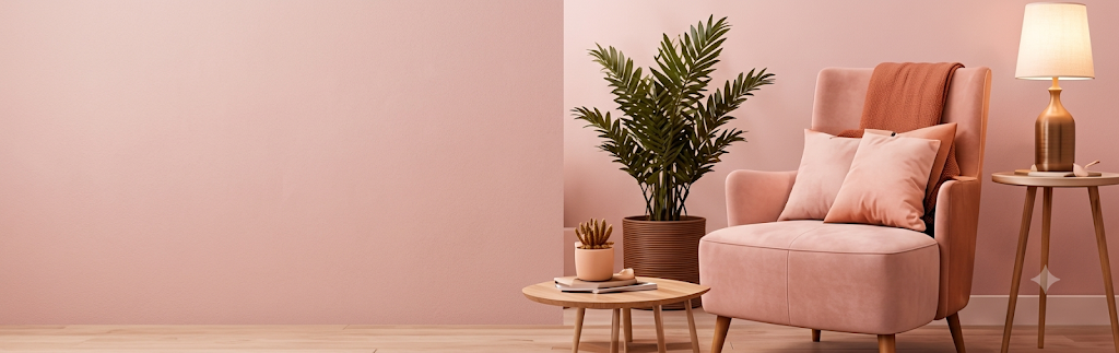 Pink armchair with cushions, a potted palm, side tables and a brass table lamp against a blush wall